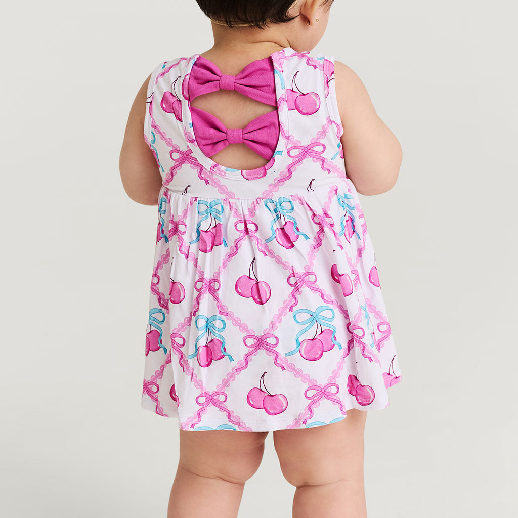 Baby wearing a dress with pink bows and cherries on a white background