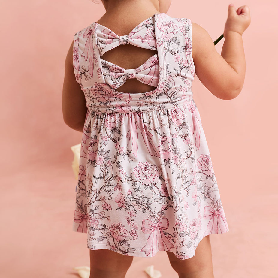 Child wearing a floral dress with bow details on a pink background