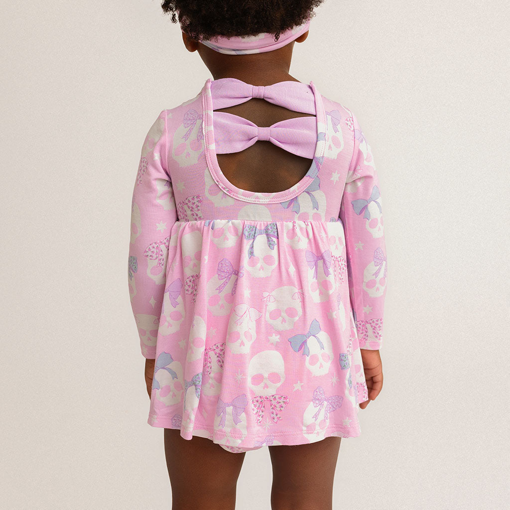 Back view of a child wearing the Posh Peanut Ms. Kelly Bow Back Bodysuit Dress, showing the back cutout with bow details, white background