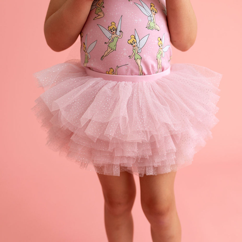Child wearing a pink fairy-themed top with pink tutu on a pink background
