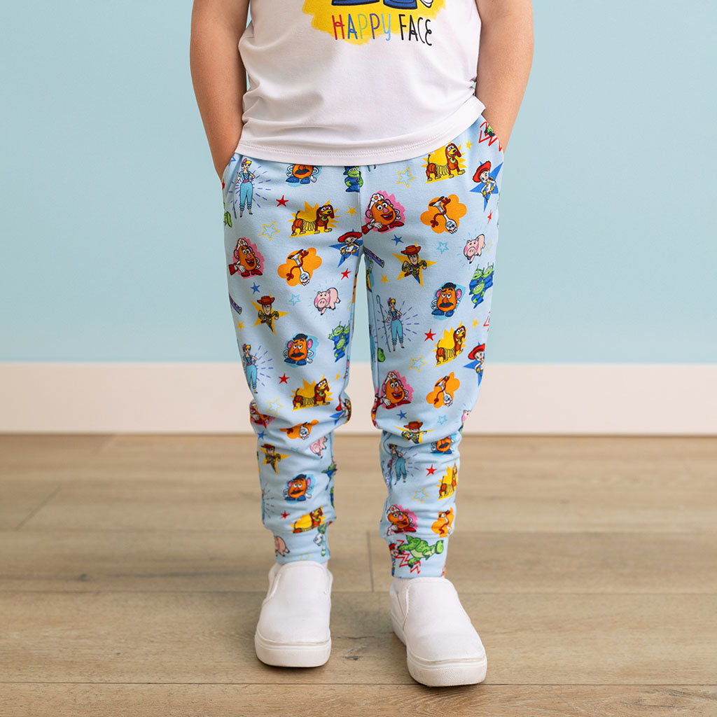 Child wearing colorful cartoon-themed pants on a wooden floor with a light blue wall background