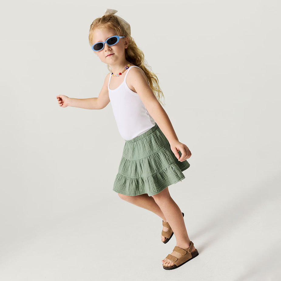 Young girl wearing a white top and green skirt on a plain background