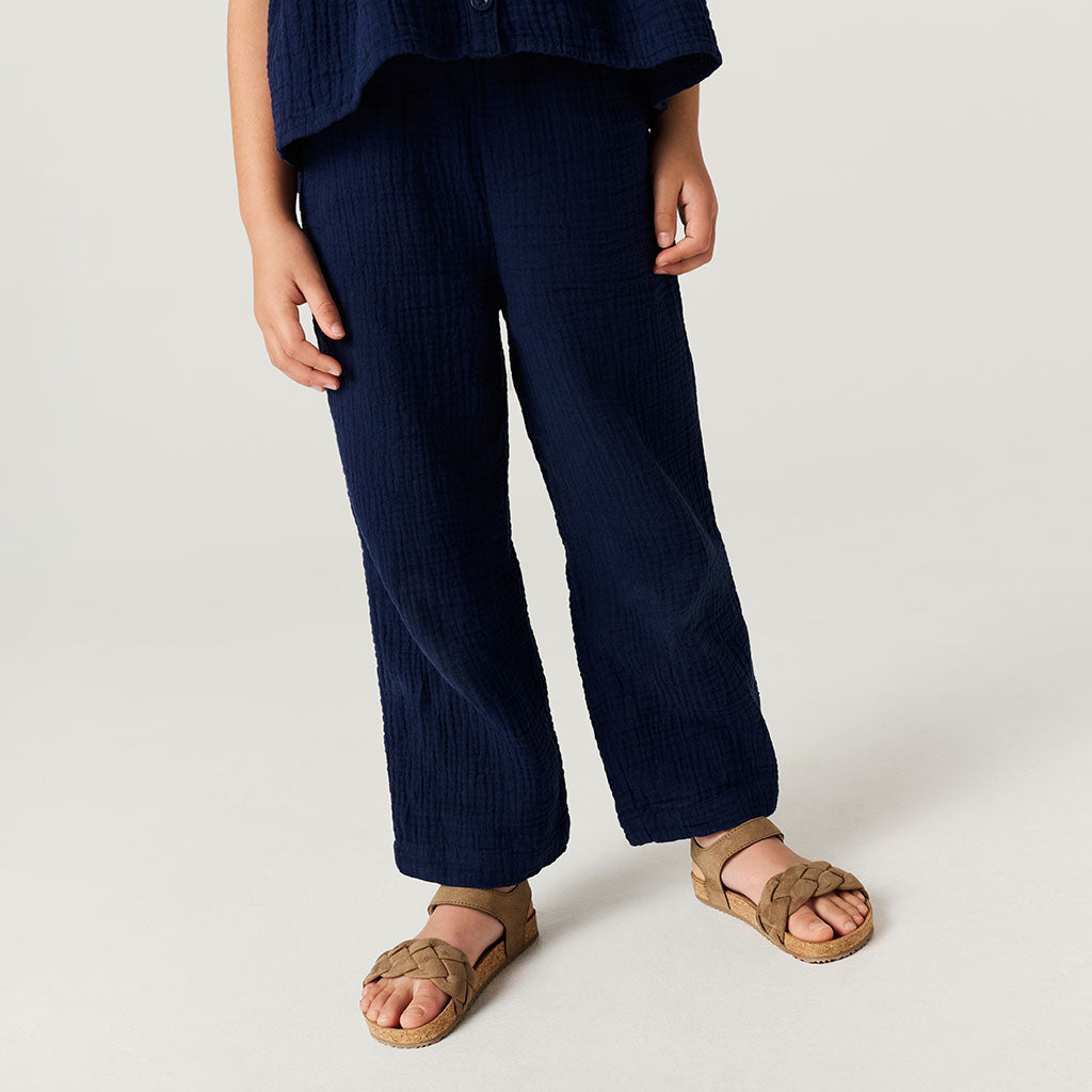 Person wearing navy blue pants and brown sandals on a white background