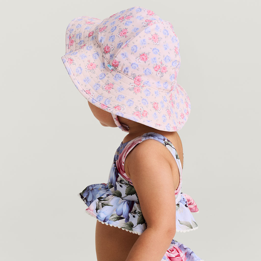 Child wearing a floral sun hat and swimsuit on a light gray background