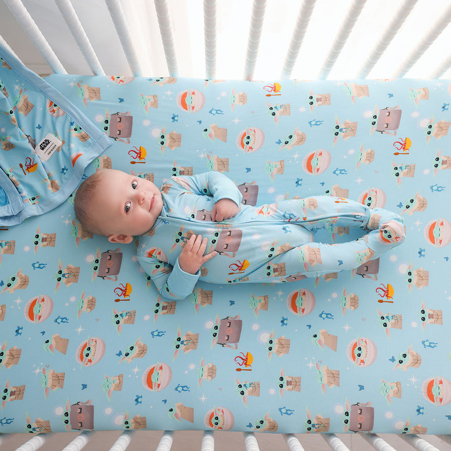 Baby lying on a crib with a patterned Star Wars Grogu mattress cover