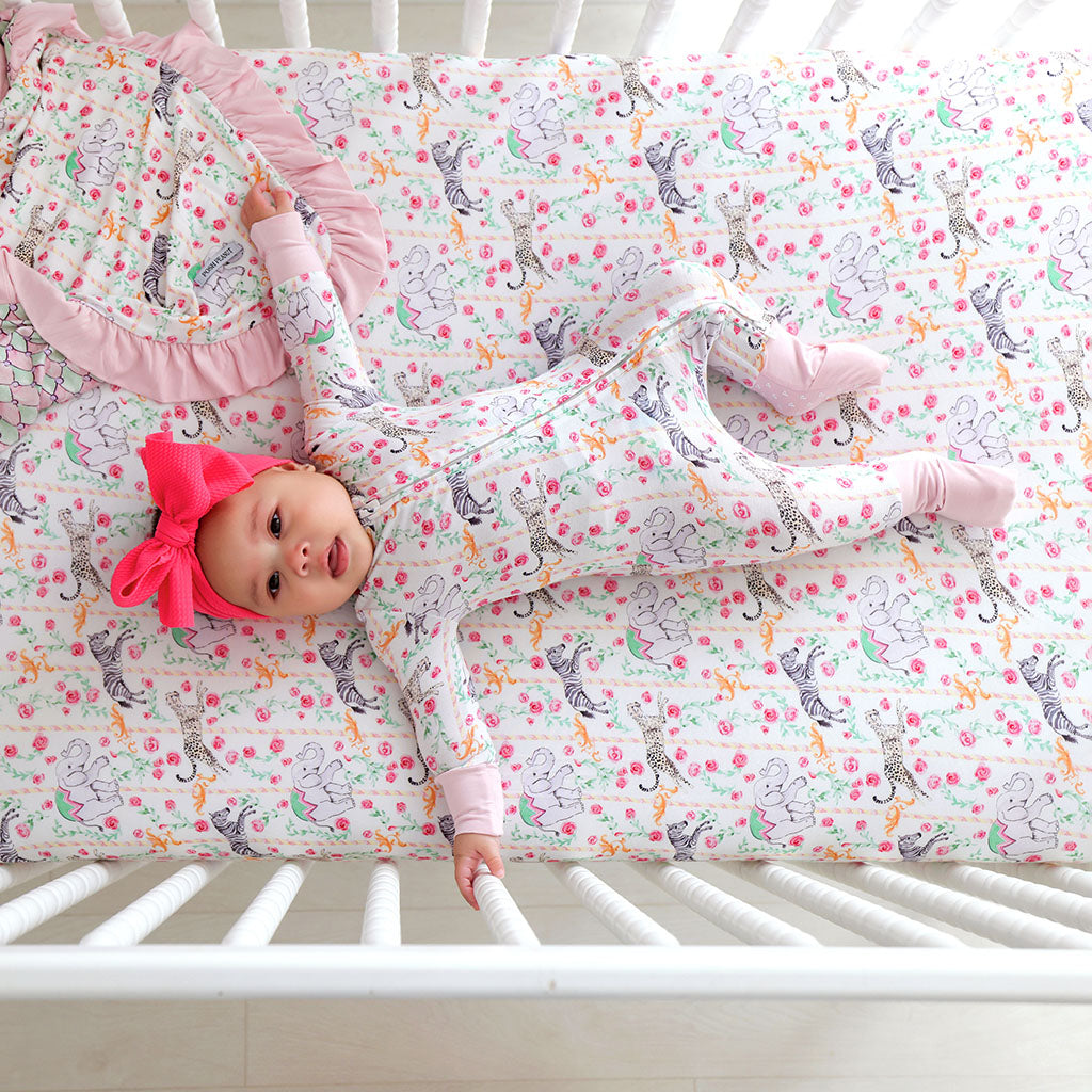 Baby lying on a crib with a colorful patterned sheet and pink headband.