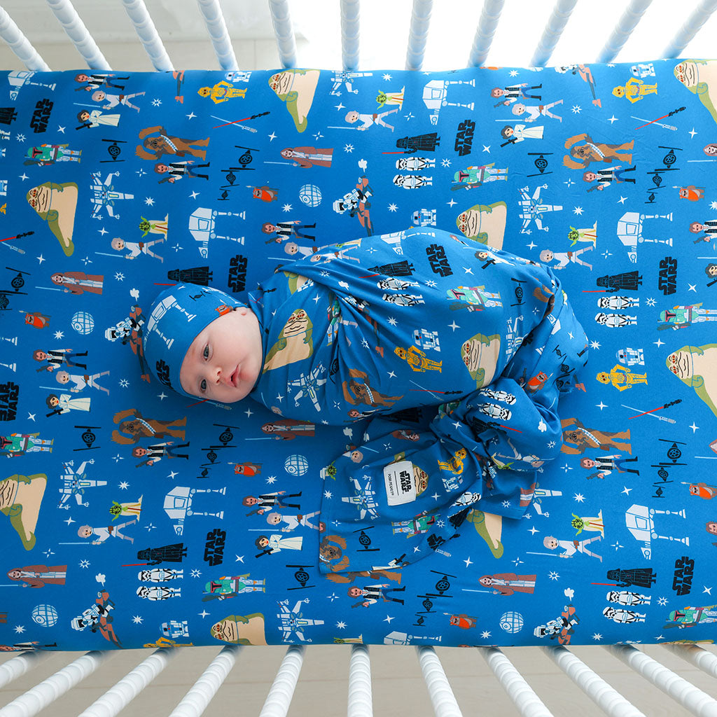 Baby wrapped in a blue Star Wars-themed blanket lying on a crib with the same pattern.