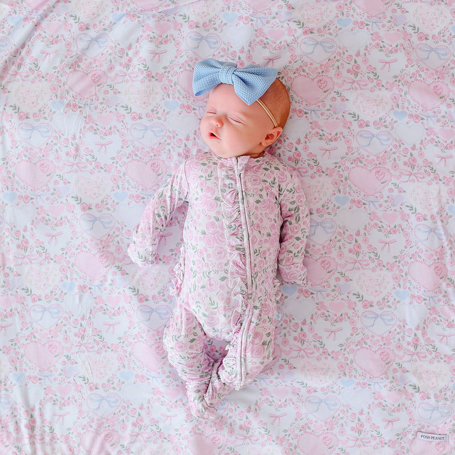 Newborn baby in a floral one piece and headband lying on a floral blanket