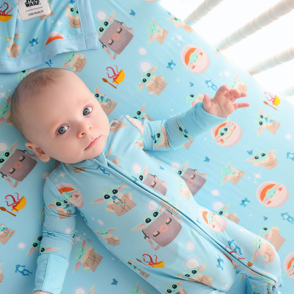 Baby lying on a crib with a blue Star Wars Grogu patterned sheet