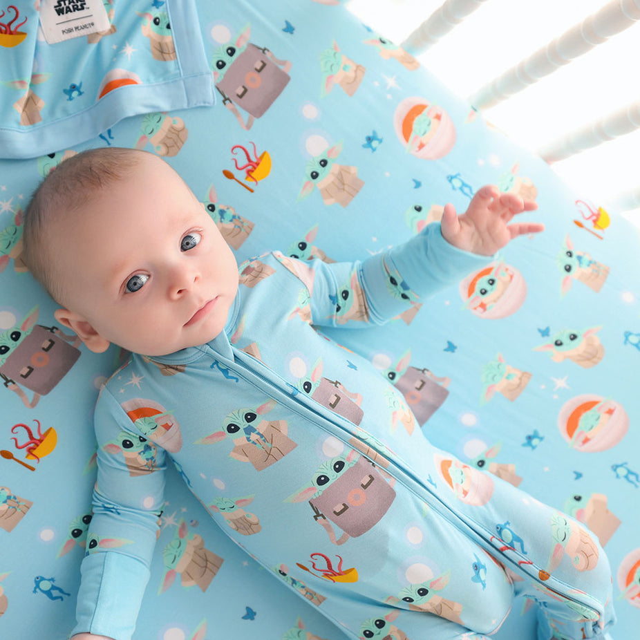 Baby lying on a crib with a blue Star Wars Grogu patterned sheet