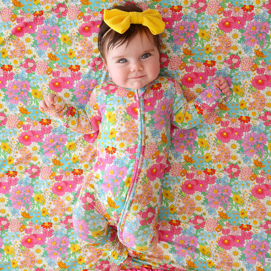Baby in a colorful floral one piece with a yellow bow on a similarly patterned background