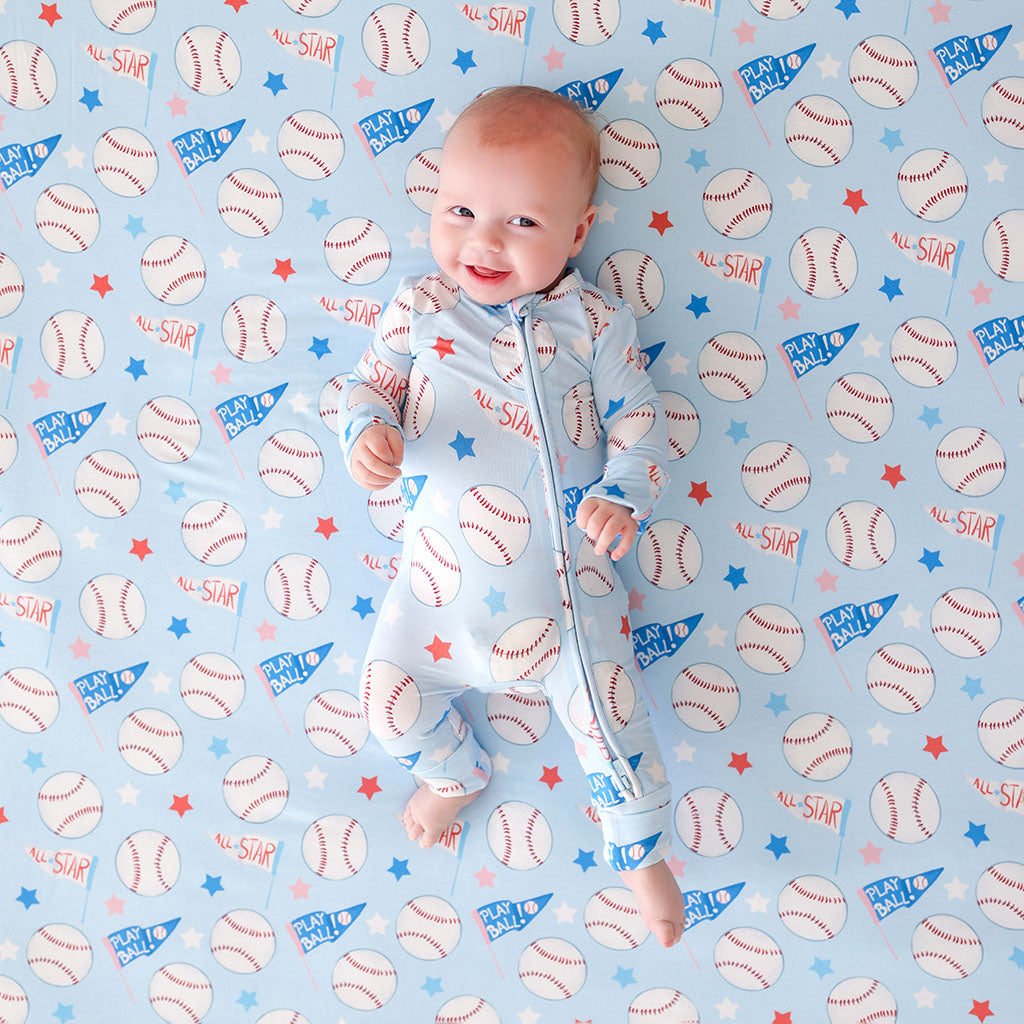 Baby in a one piece with baseball-themed pattern on a blue background