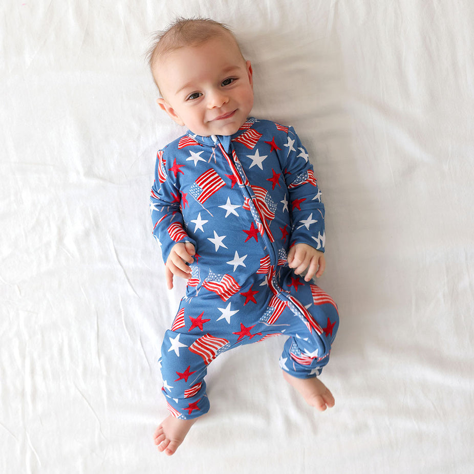 Baby wearing a blue onesie with American flag pattern on a white blanket