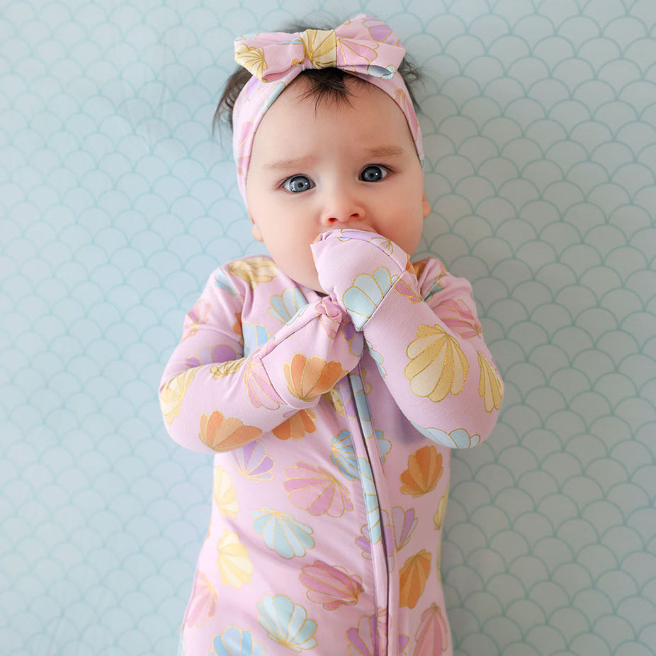 Baby wearing a pink floral outfit and headband against a light blue patterned background