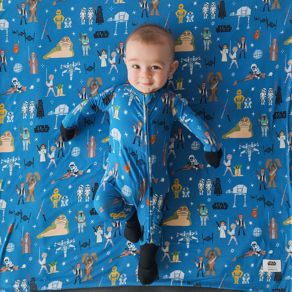 Child wearing a blue Star Wars-themed onesie on a matching fabric background