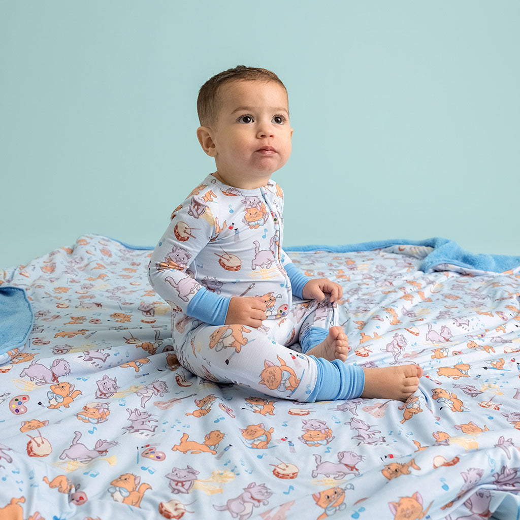 Child sitting on a blanket wearing a matching Disney The Aristocats Berlioz and Toulouse printed convertible one piece.