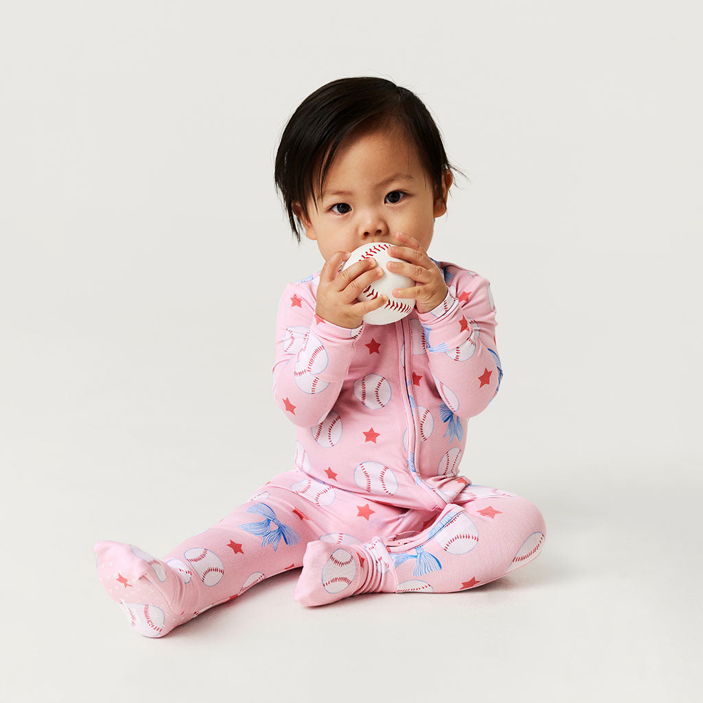 Baby in pink one piece with animal patterns sitting on a light gray background