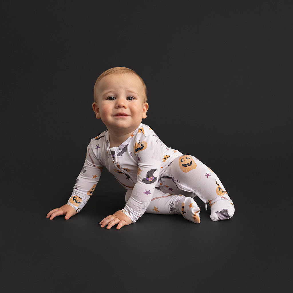 Baby crawling on a dark background, wearing the Posh Peanut Irving Convertible One Piece with the scattered Halloween-icon print.