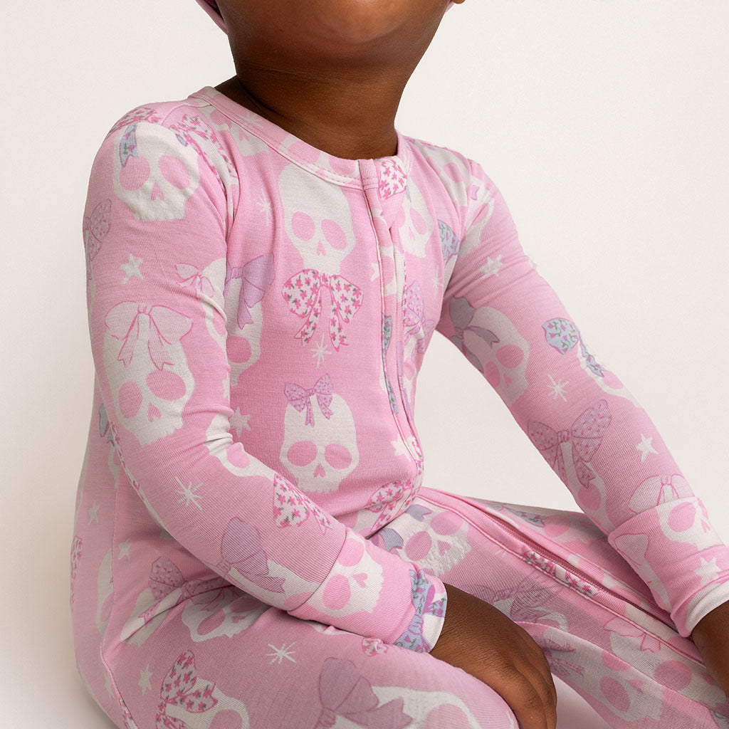 Close-up of a child wearing the Posh Peanut Ms. Kelly Convertible One Piece, pink with white skull print, white background
