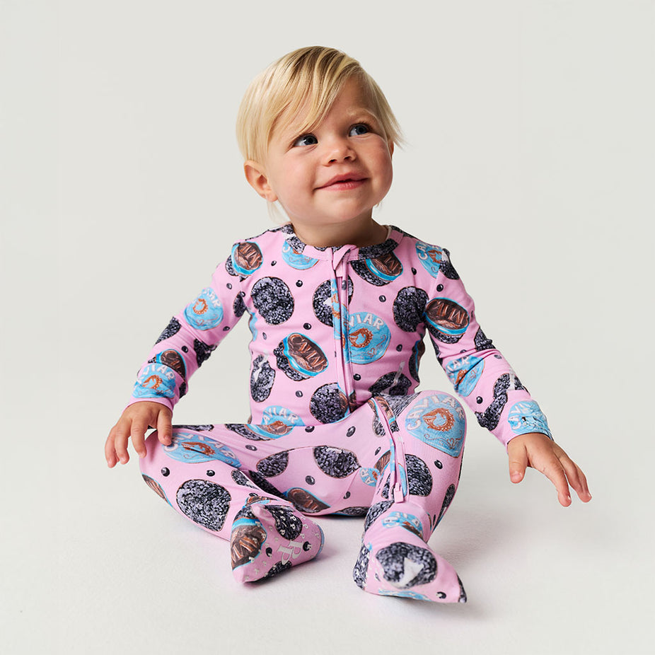 Child wearing a pink one piece with caviar pattern on a light gray background