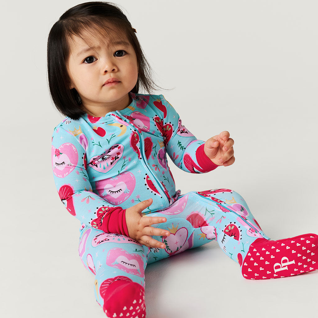 Child wearing a colorful one piece with heart and eyes pattern on a light gray background