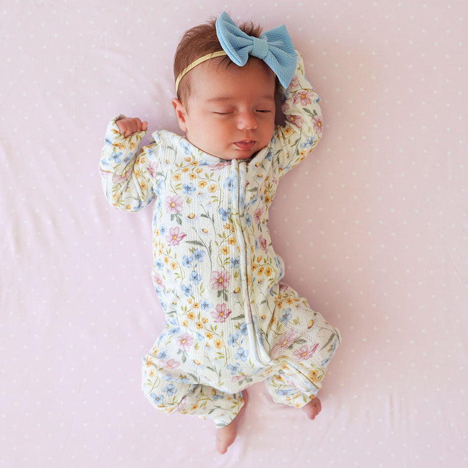Newborn sleeping, wearing the Posh Peanut Hazel Pointelle Convertible One Piece, headband, pink background