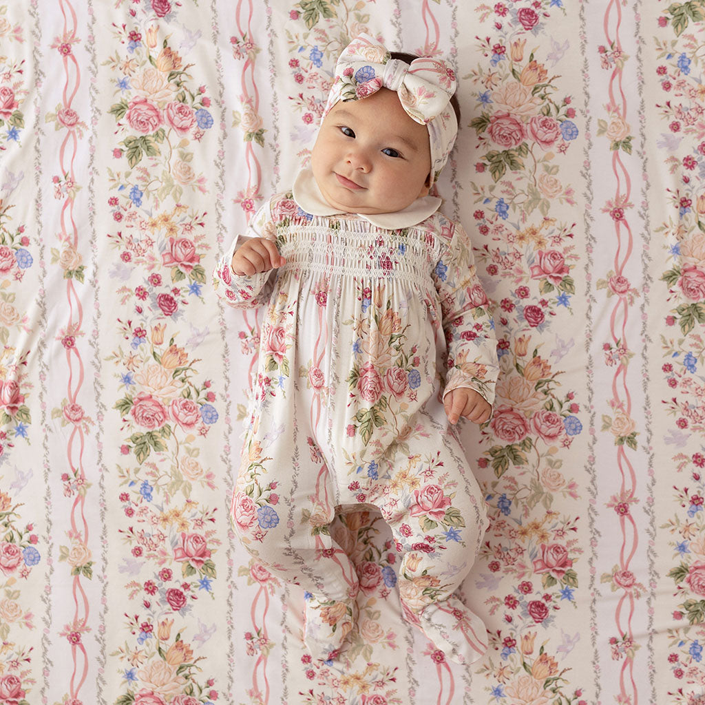 Baby lying on a Janey print fabric backdrop, wearing a matching floral footie with a bow headband