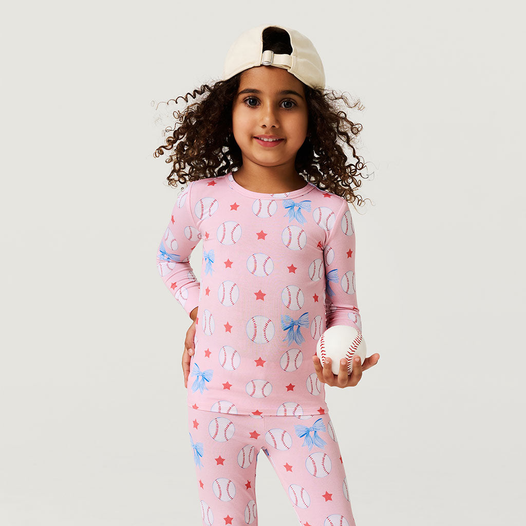 Child wearing a pink pajama set with sports-themed design, holding a baseball.