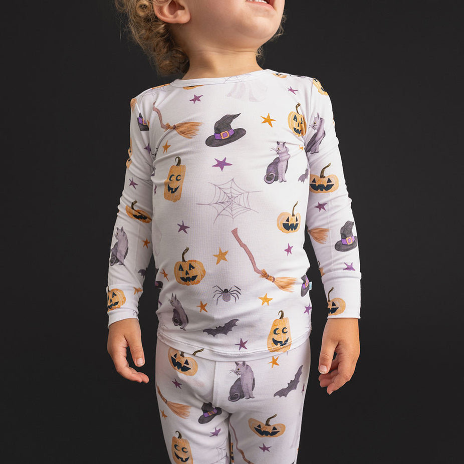 Close-up of a child wearing the Posh Peanut Irving Classic Pajama Set, showing the long-sleeve top with scattered Halloween icons on white.