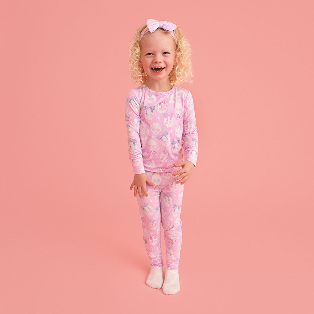 Child standing, wearing the Posh Peanut Ms. Kelly Classic Pajama Set, pink background