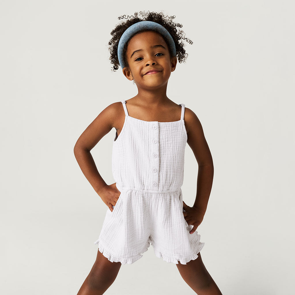 Young girl wearing a white romper against a plain background