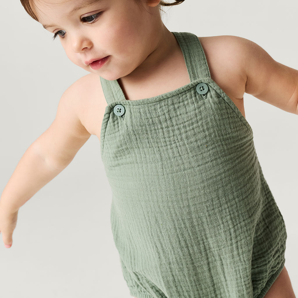 Child wearing a green textured romper against a plain background