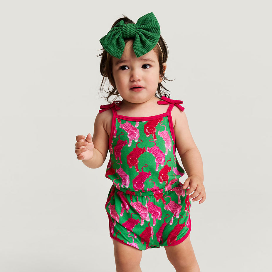 Child wearing a green and pink romper with a large green bow on a plain background