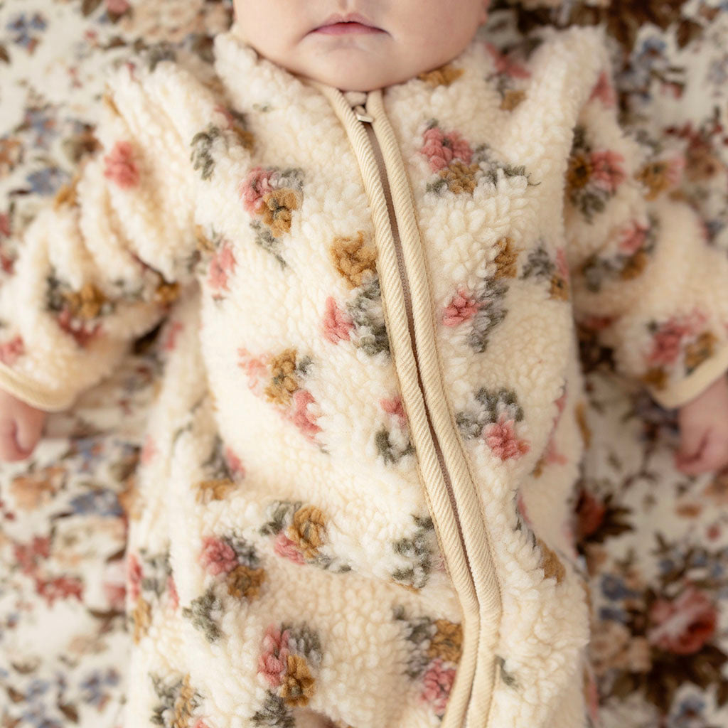 Baby lying down, close-up on face, wearing the Amber print sherpa romper with funnel collar, on a matching floral fabric backdrop
