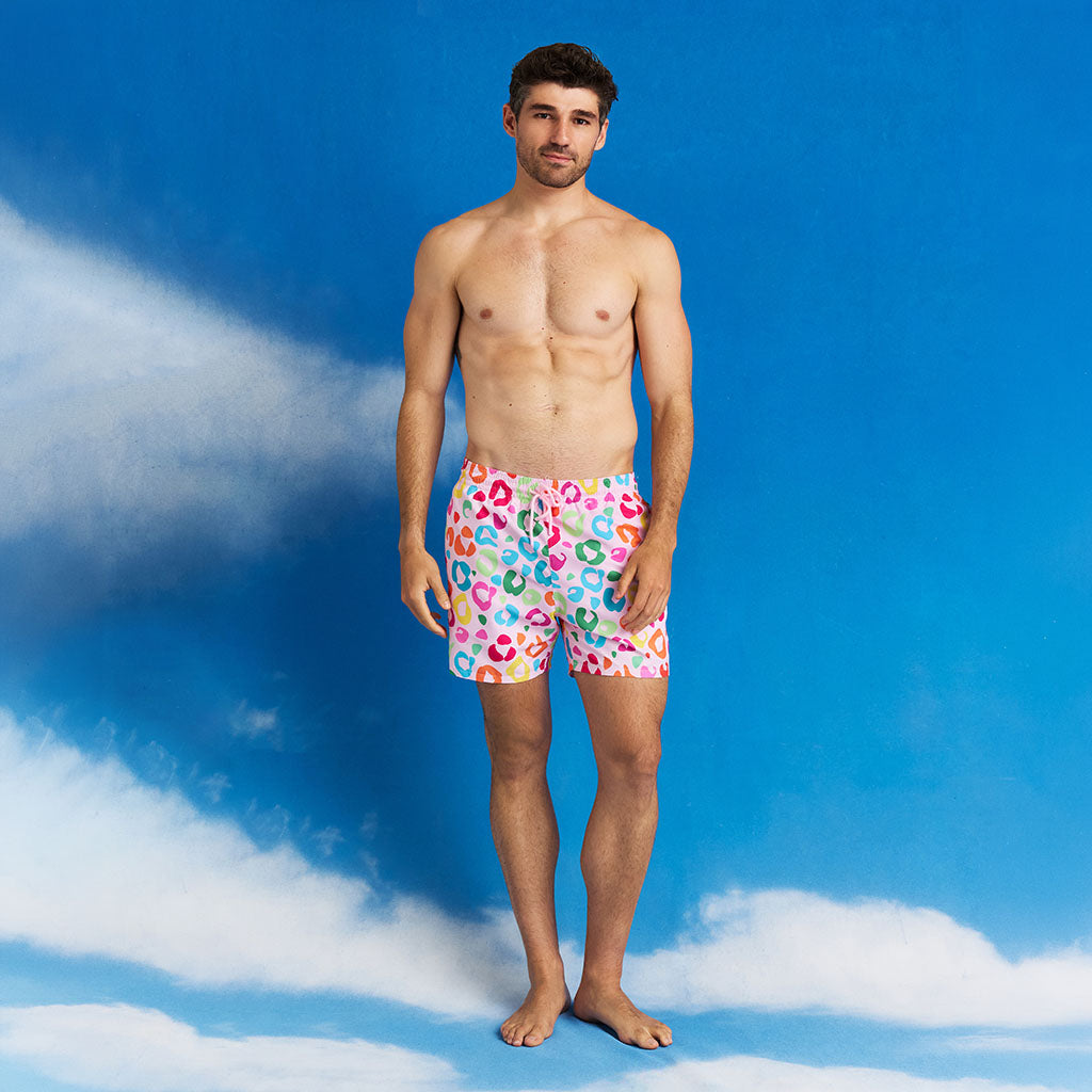 Man wearing colorful swim trunks standing against a blue sky with clouds