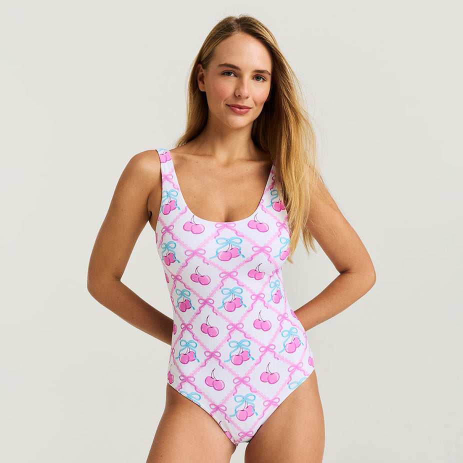 Woman wearing a pink swimsuit with cherry and bow pattern on a light gray background