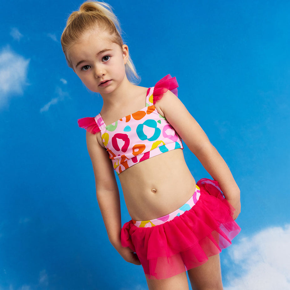 Young girl wearing a colorful swimsuit with a pink tutu against a blue sky.