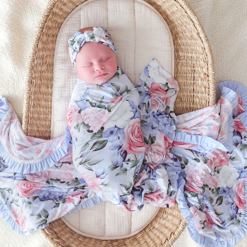 Newborn baby wrapped in a floral swaddle blanket in a wicker basket.