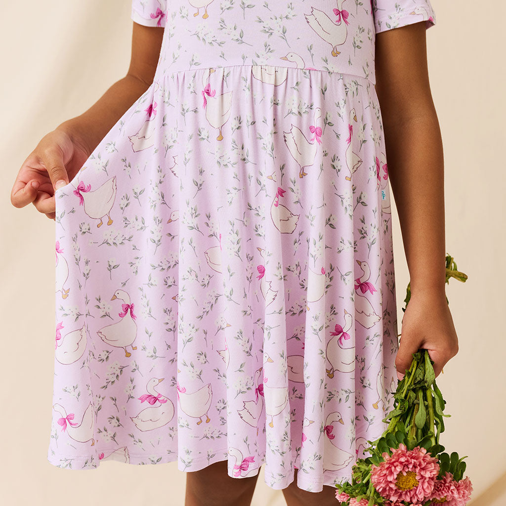 girl wearing a pink dress with duck pattern holding flowers against a beige background