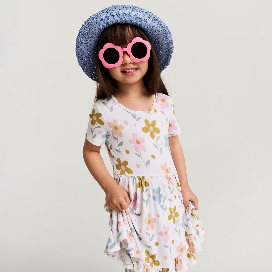 Child wearing a floral dress, pink sunglasses, and a blue straw hat on a light gray background