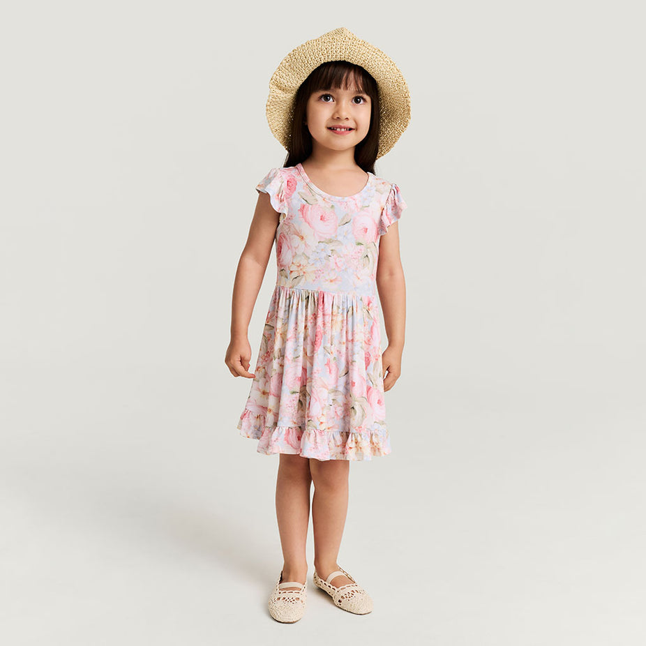Young girl wearing a floral dress and straw hat on a plain background