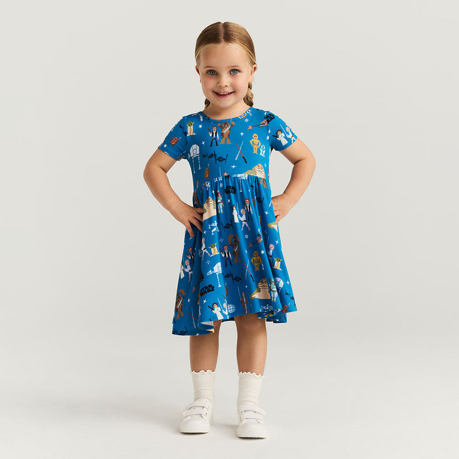 Young girl wearing a blue dress with Star Wars print on a light gray background