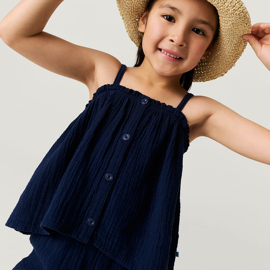 Young girl wearing a navy blue top and straw hat on a light gray background