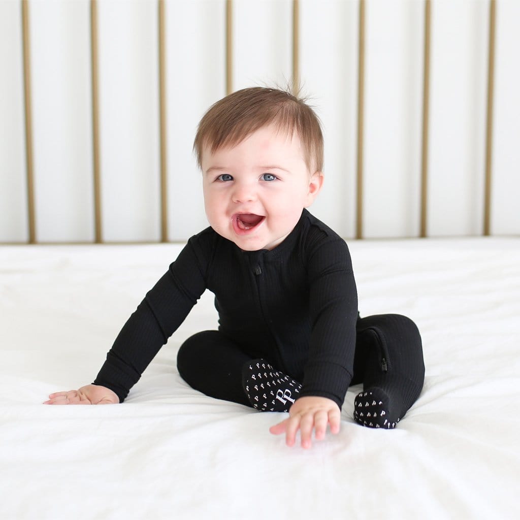 Baby on bed wearing Cadet Footie Ruffled Zippered One Piece